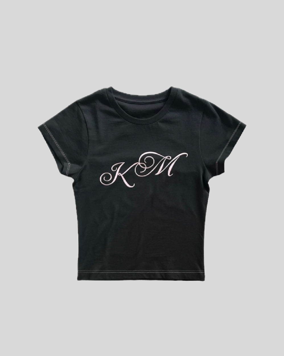 Sort T-shirt med korte ærmer og dekorativt "KM" print i script-font centralt på forsiden.